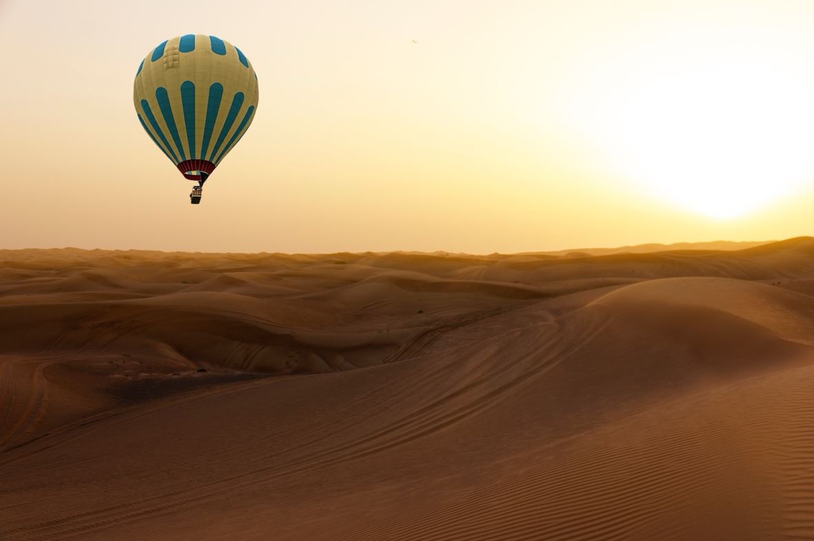 Hot air balloon flying over desert dunes near Dubai at sunrise, symbolizing international immigration opportunities for Dubai residents