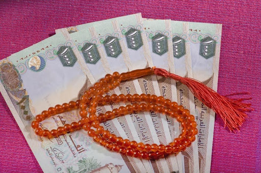 U.A.E. dirham banknotes with prayer beads representing Shariah-compliant EB-5 investment for Dubai investors working with US immigration lawyers