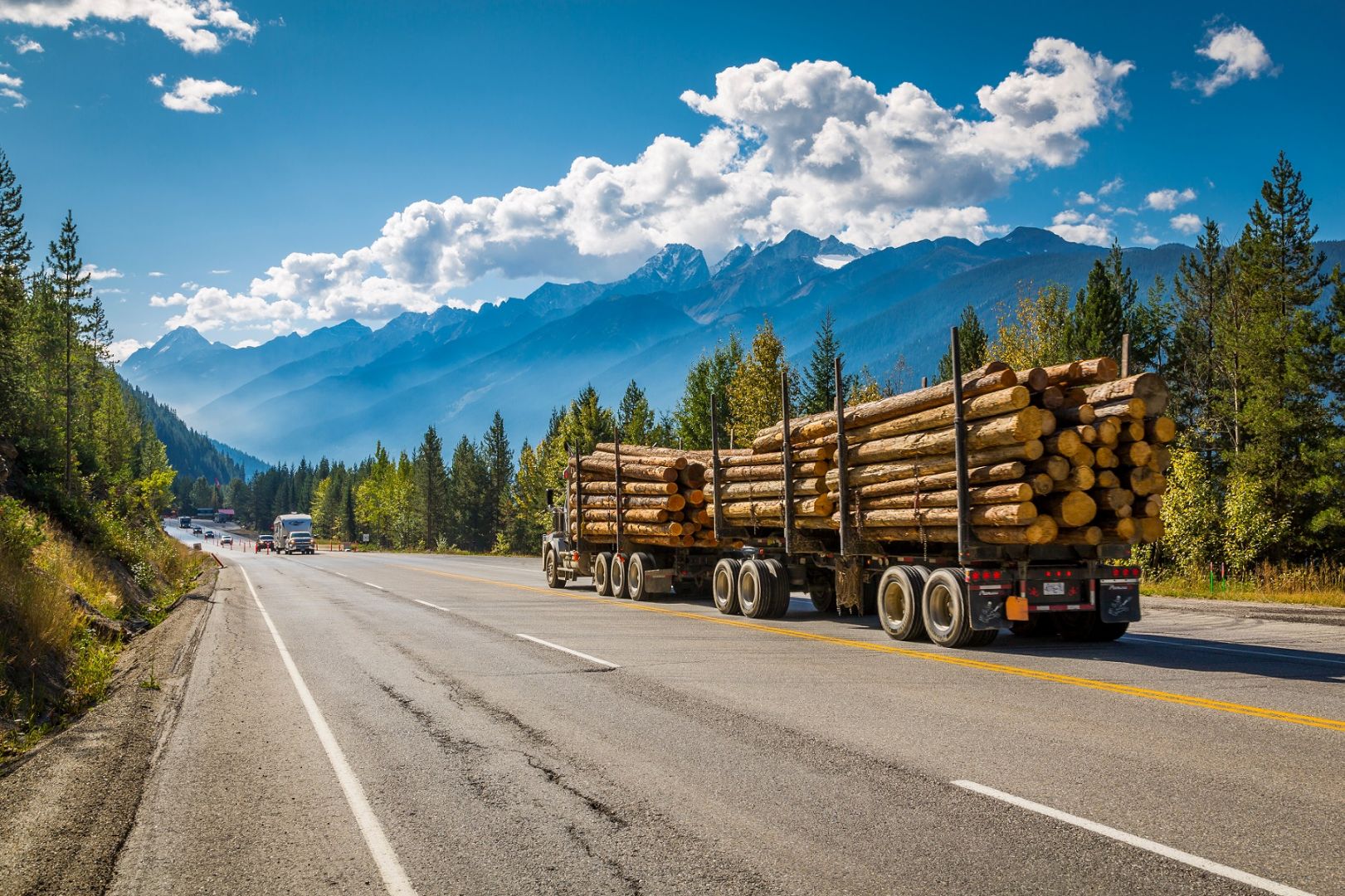 Canadian logging truck transporting timber along a mountain highway, representing a Canadian trucking company expanding operations to the United States using the E-2 investor visa